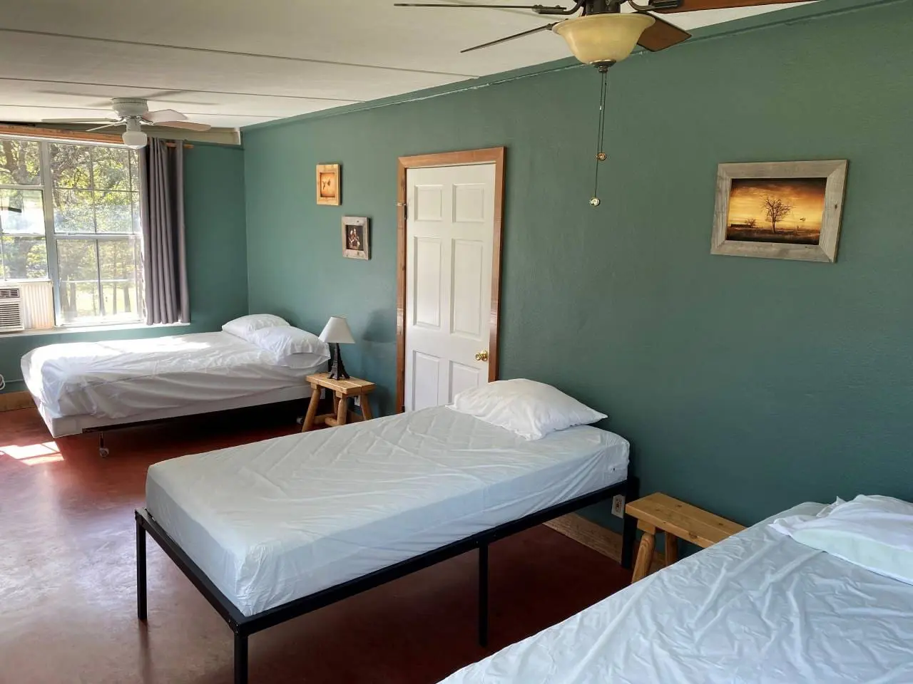 A simple room with teal walls, two single beds with white bedding, a closed white door, and a painting on the wall.