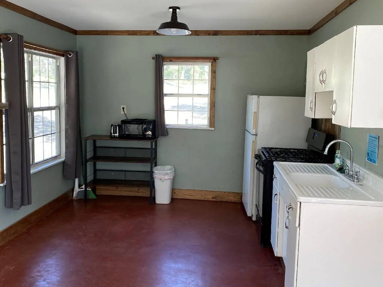 Interior of a small kitchen with green walls, featuring a white refrigerator, stove, sink, and black shelving unit. two windows provide natural light.