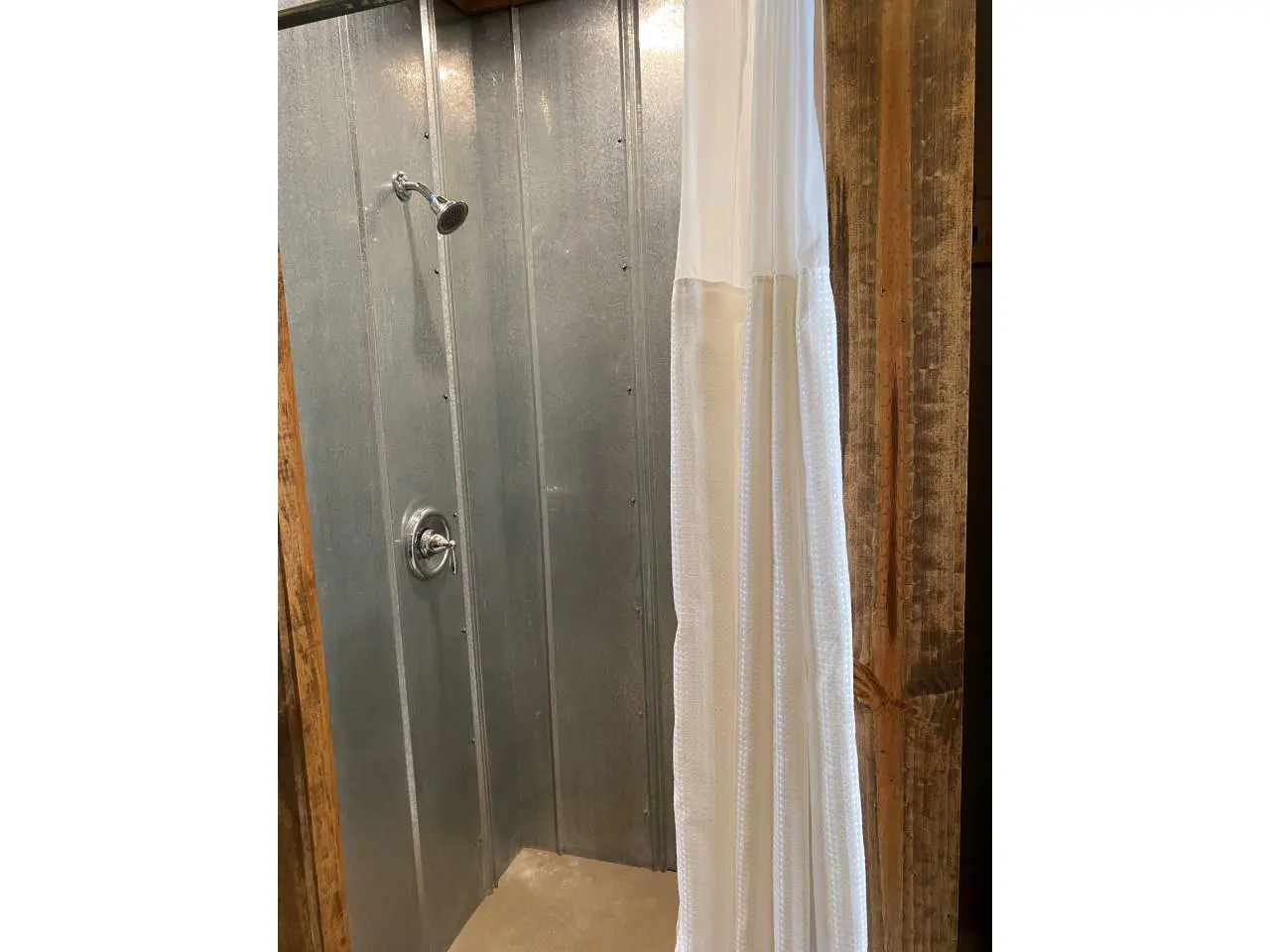 Rustic style bathroom with a corrugated metal shower and a white curtain on the right, hanging from a ceiling-mounted rod.