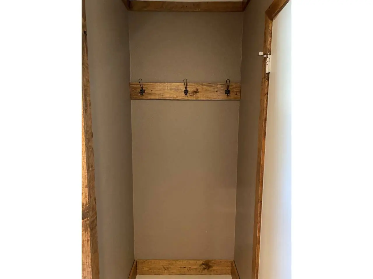 An empty wooden coat closet with a row of hooks on a beige wall, bordered by wooden frame.