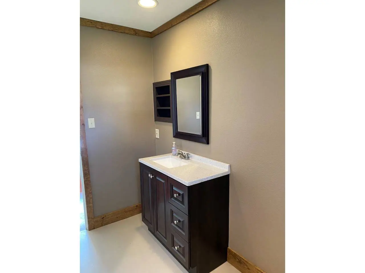 A small bathroom featuring a dark wooden vanity with a sink and mirror, set against a beige wall under natural light.