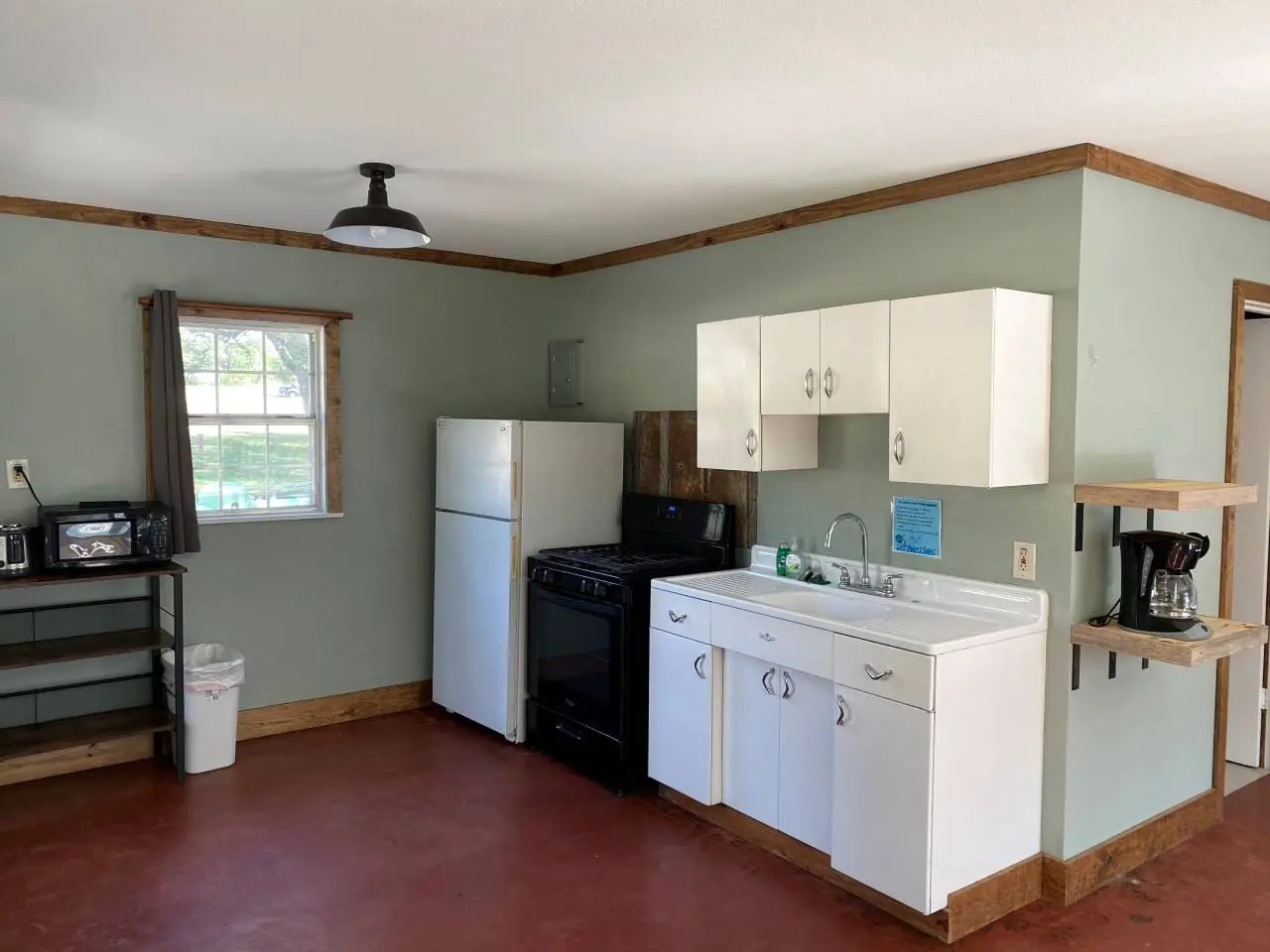 A small kitchen with mint green walls, white cabinets, a black stove, a refrigerator, and a coffee maker on a wooden counter.