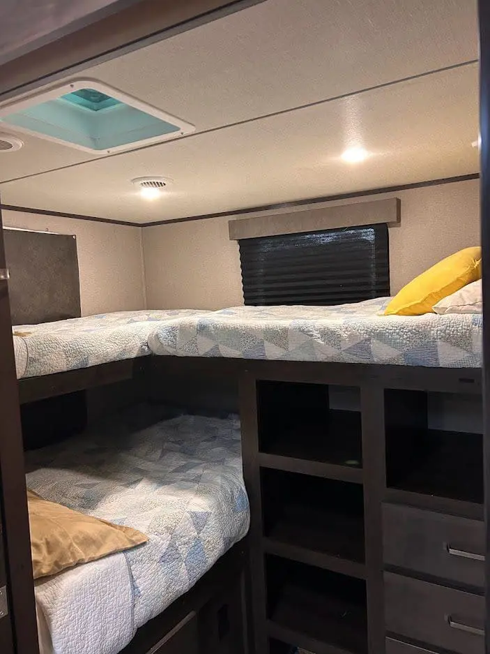 Interior of a camper with stacked bunk beds, thematic bedding and storage shelves; natural light from overhead.