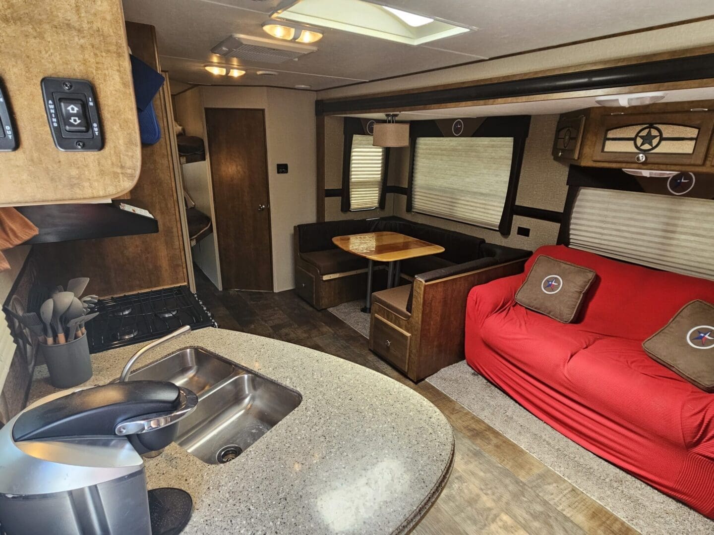 Interior of a modern rv featuring a kitchen sink, red sofa, wooden table, and multiple storage compartments.