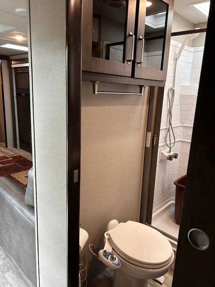 Interior view of a compact rv bathroom featuring a toilet, shower, and storage cabinets, viewed from the doorway.