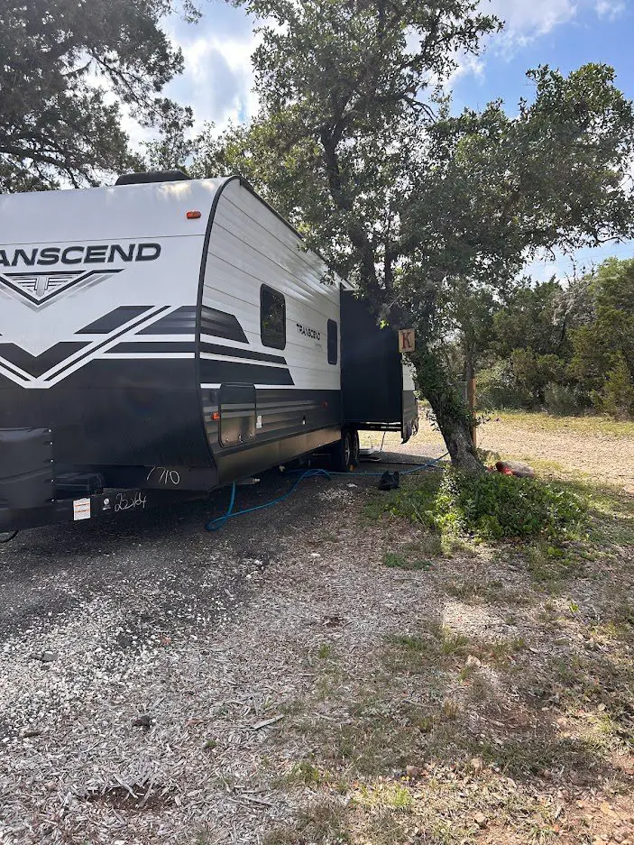 A travel trailer parked in a rustic outdoor setting with trees and sunlight.