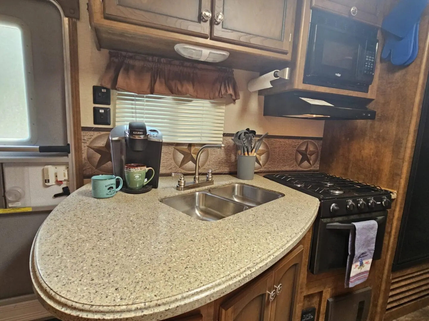 Interior of a compact rv kitchen with modern appliances, a curved countertop, sink, stove, microwave, and coffee maker.