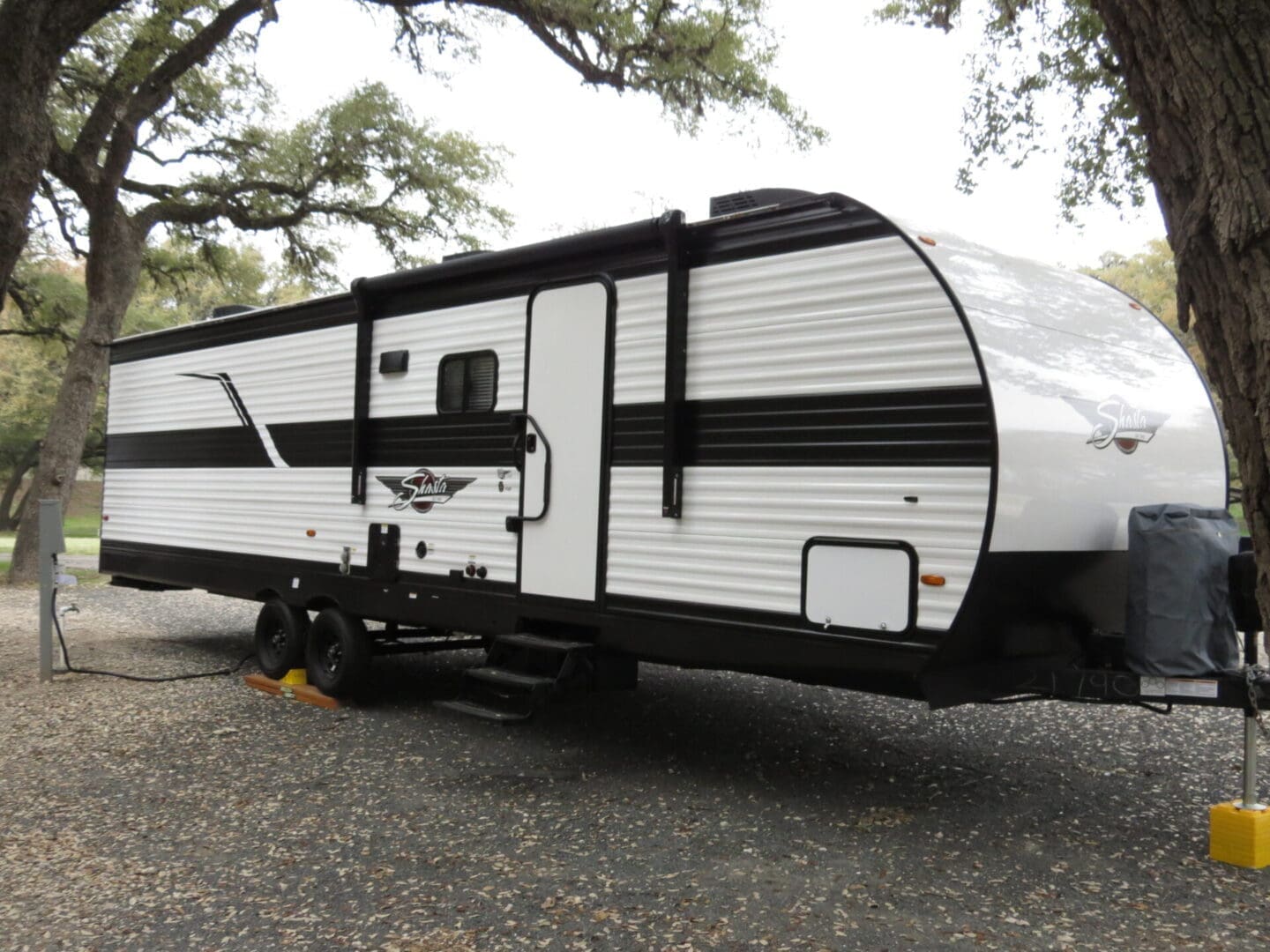 A white and black travel trailer parked under trees in a serene outdoor setting.