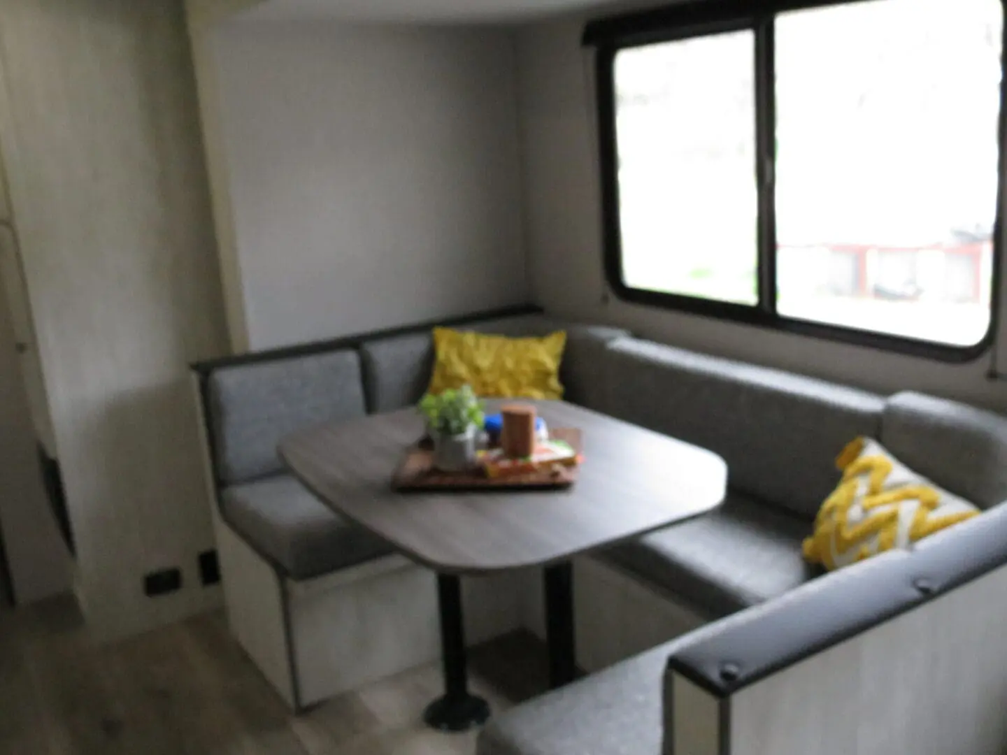 A blurry interior image of an rv with a gray u-shaped sofa, a wooden table, and decorative pillows.