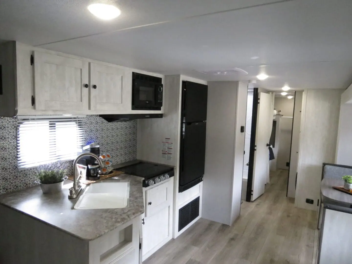 Interior of a modern rv showing a compact kitchen with appliances and a hallway leading to other sections.