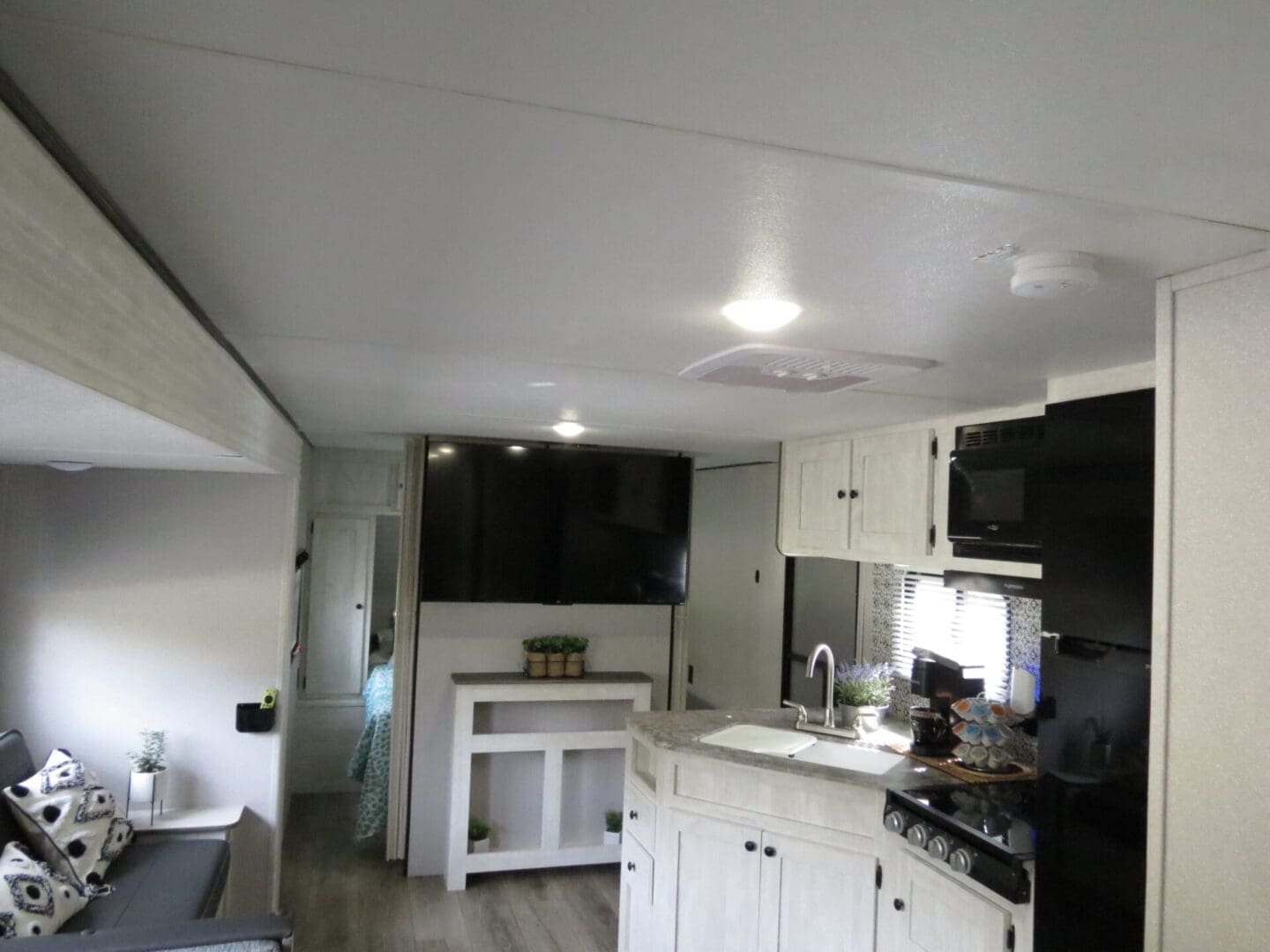 Interior of a modern camper with a kitchen on the right, featuring white cabinets and a counter, and a living area with a sofa on the left, under ambient lighting.