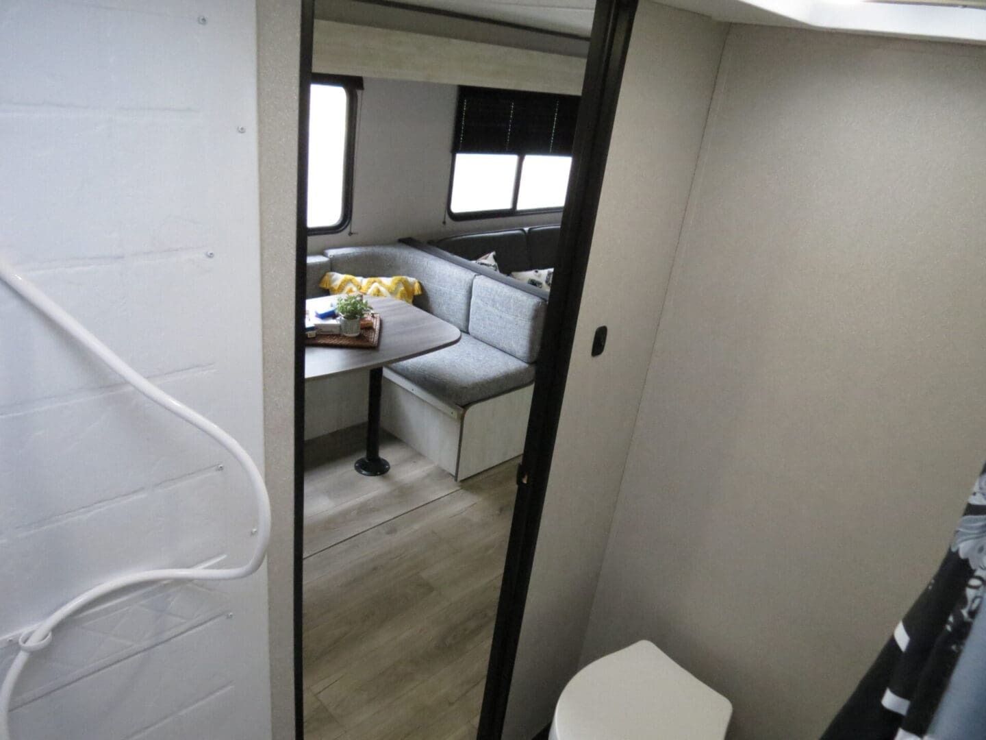 Interior of a compact rv showing a small dining area with a bench seat and table, positioned beside a window. the entrance to the bathroom is visible on the right.