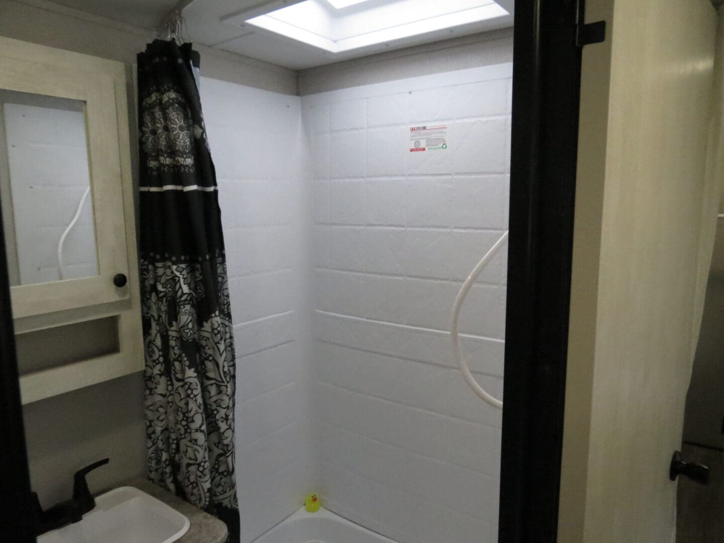 Small bathroom with a shower curtain, sink, and mirror in a compact space with white walls and fluorescent lighting.