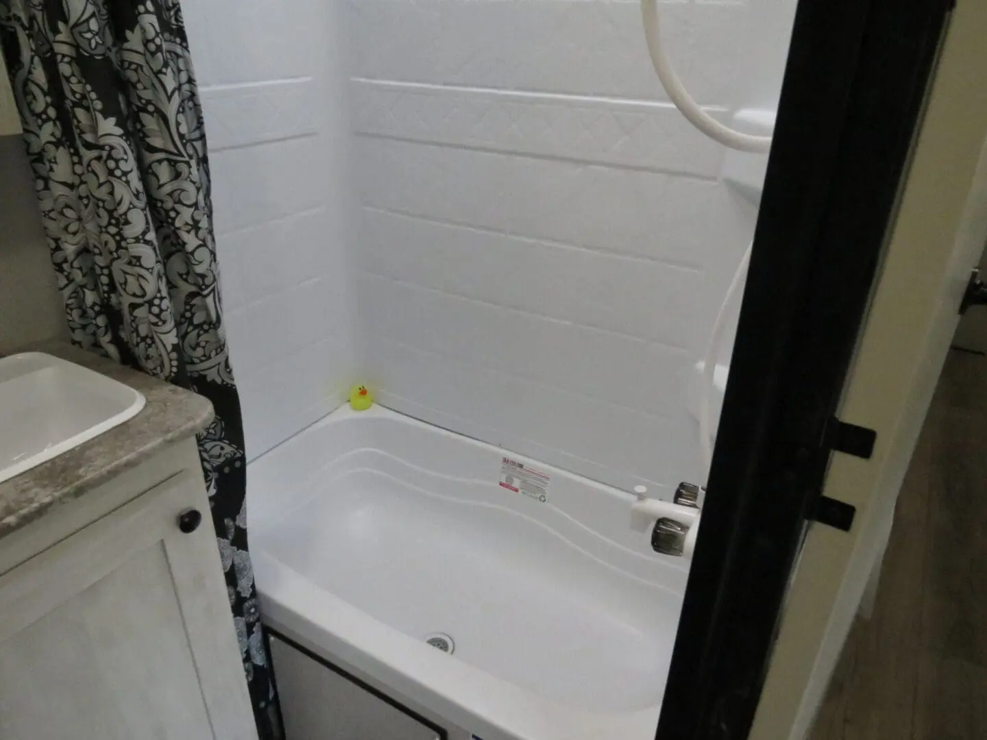 A small bathroom featuring a white bathtub with a yellow rubber duck, shower curtain to the left, and a sink with a vanity on the right.