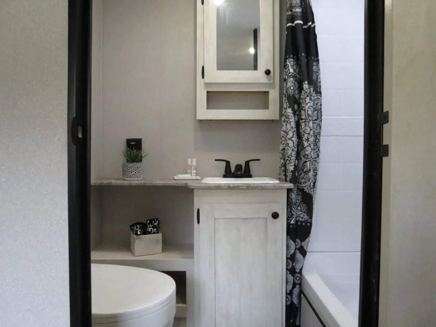 A small modern bathroom featuring a white toilet, a vanity with a sink, a mirrored medicine cabinet, and a black shower curtain.