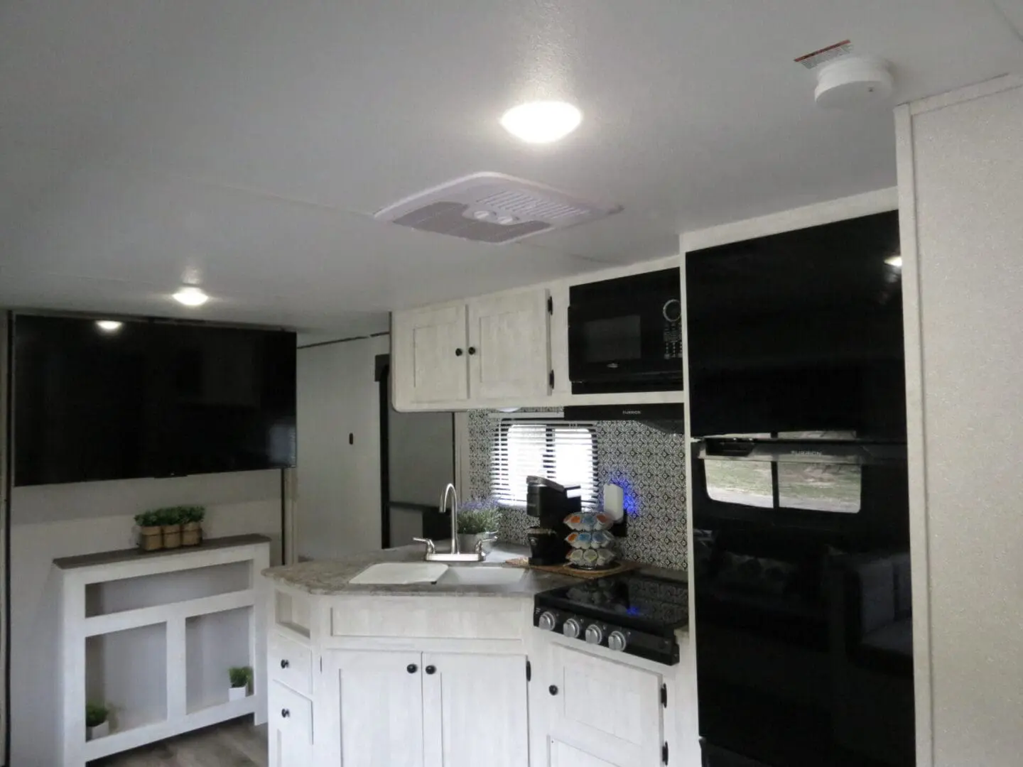 Modern rv kitchen interior with white cabinets, a stove, microwave, and a small dining area to the left.