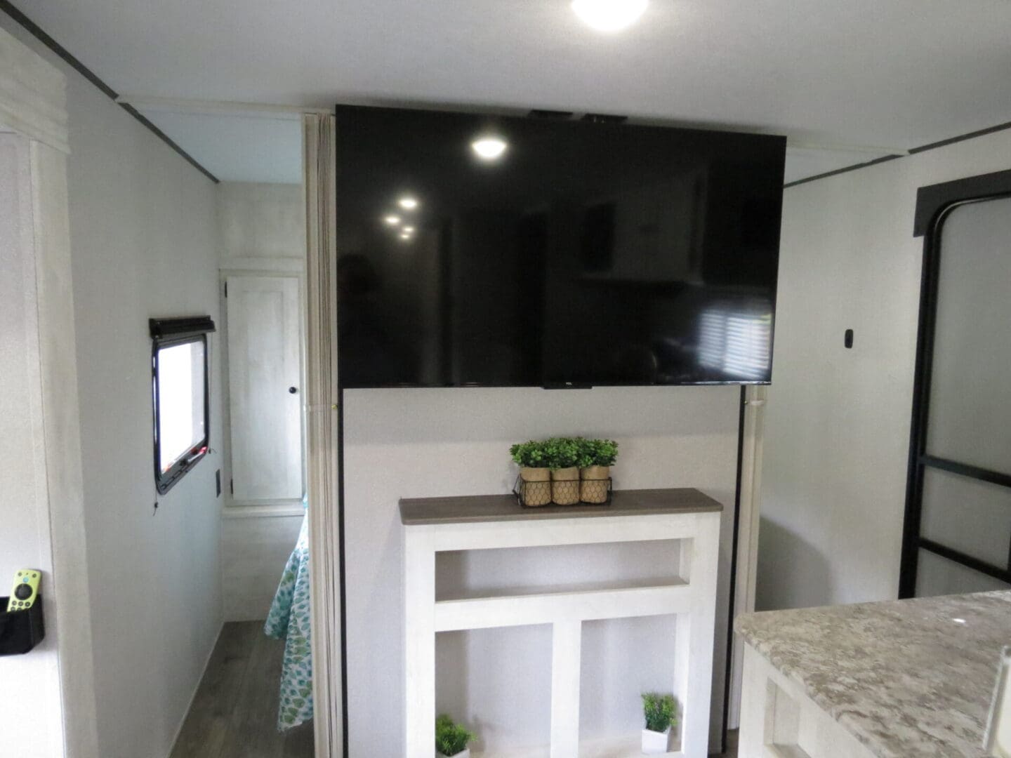 Interior of a modern rv with a large flat-screen tv mounted on the wall above a small decorative table with potted plants.