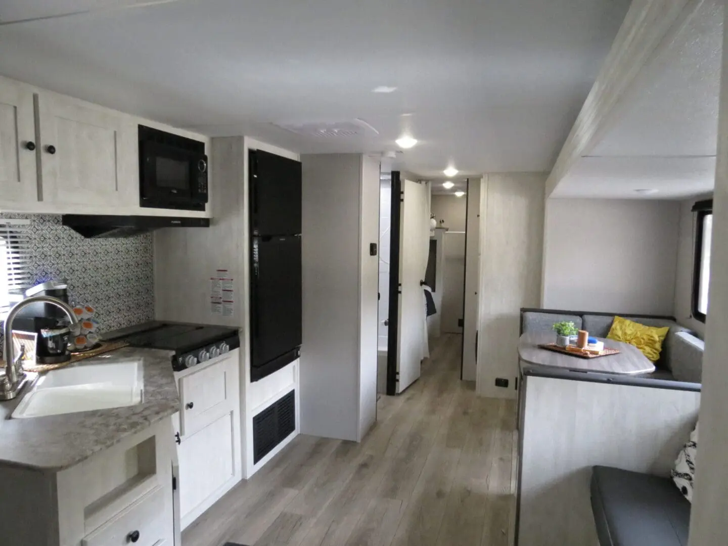 Interior of a modern rv featuring a kitchen with appliances, a couch, and a hallway leading to additional rooms.