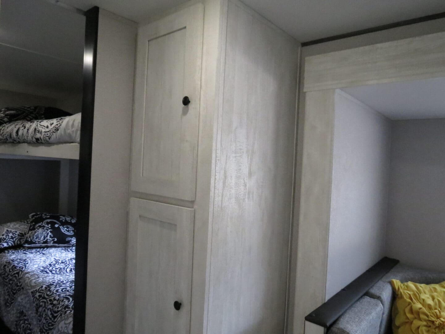 Interior of a compact living space showing a bunk bed with patterned bedding and a built-in wardrobe, designed in light wood tones.