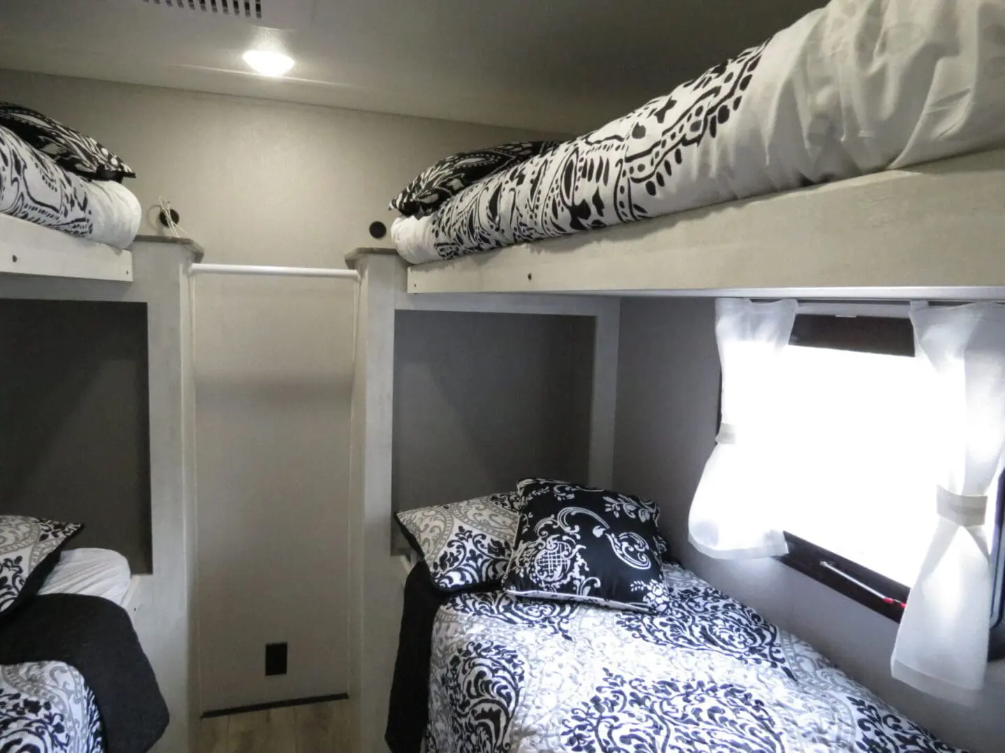 Interior of a small room with two bunk beds, featuring black and white bedding, and a window with blinds.