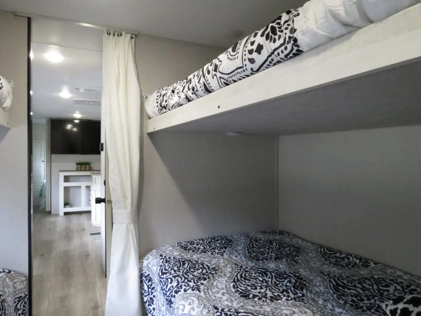 Interior of a modern rv with a bunk bed setup featuring patterned bedding, gray walls, and a curtain divider.