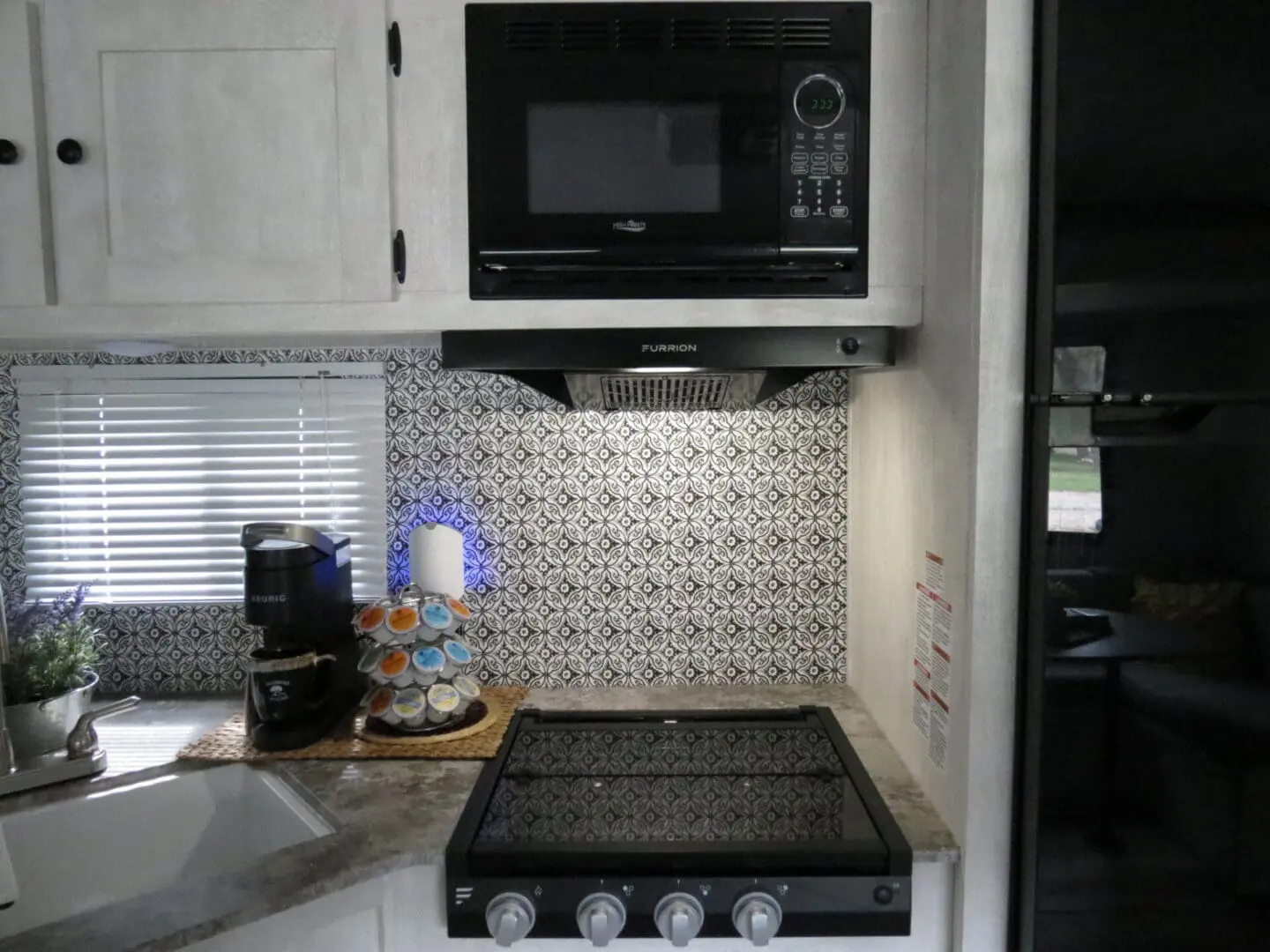 A compact kitchen inside an rv featuring a microwave, stove, coffee maker, and patterned backsplash.