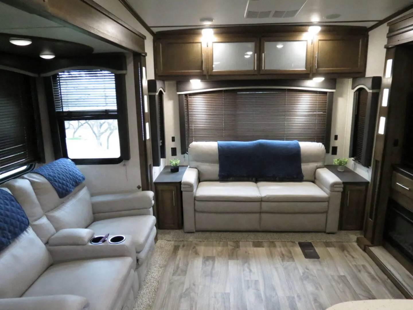 Interior of a modern rv featuring a sofa, two recliners, and wooden cabinets.