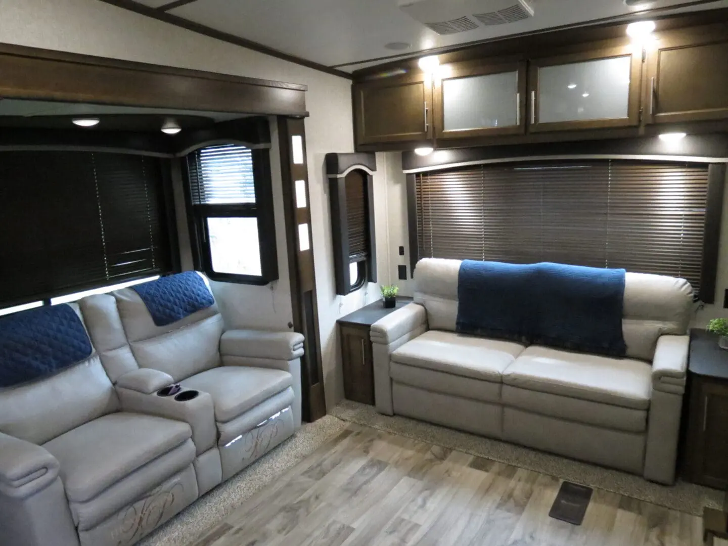 Interior of a modern rv featuring two sofas, wooden cabinets, and blinds over the windows.