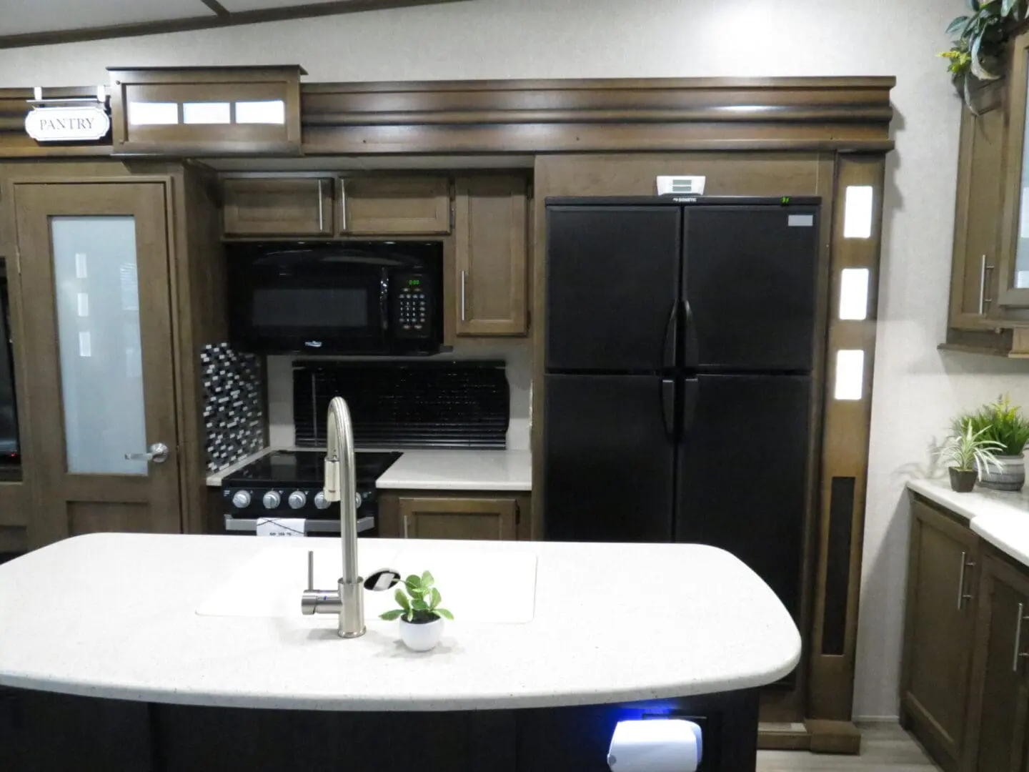 Interior of a modern rv kitchen featuring a curved countertop with a sink, a refrigerator, microwave, and a stove, all set against wooden cabinetry.