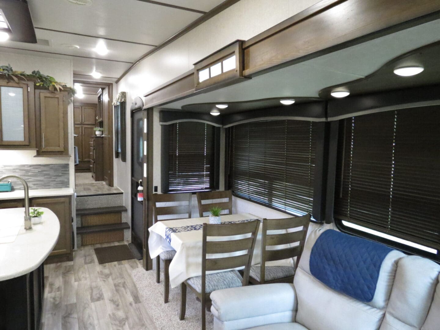 Interior of a modern rv with a dining area, kitchen, and hallway leading to the back rooms, featuring contemporary decor.