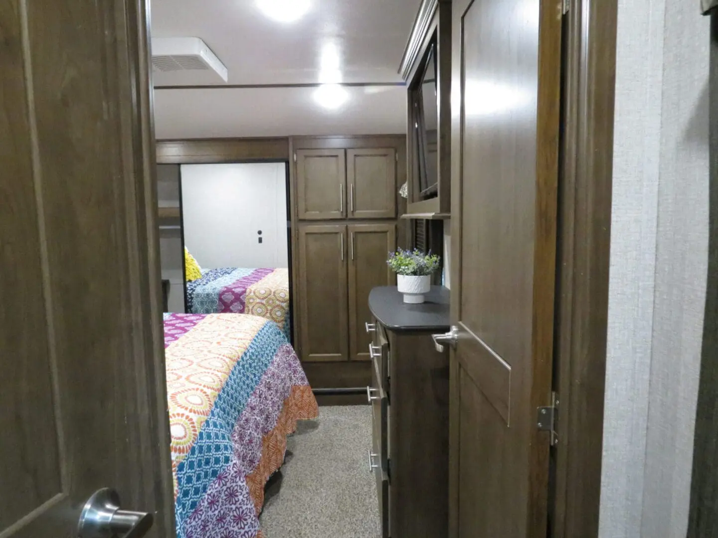 Interior view of a modern rv bedroom featuring a colorful quilt on a bed, wooden cabinets, and a small plant on a ledge.