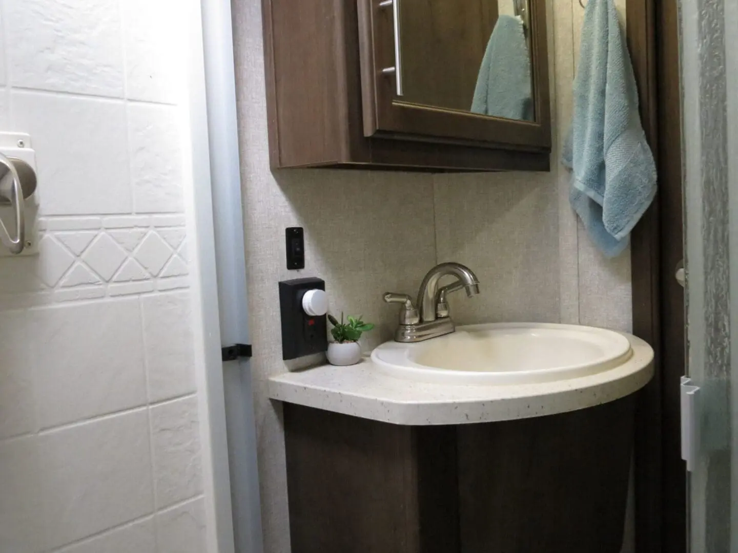 A small bathroom featuring a white sink with a silver faucet, dark wood cabinets, a hanging teal towel, and white walls.