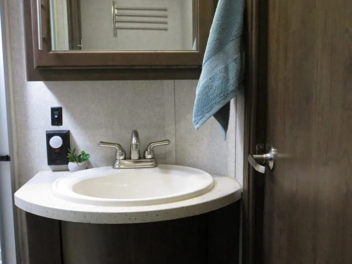 A small bathroom featuring a white sink with a chrome faucet, a mirror, a teal towel hanging on the wall, and an open door.