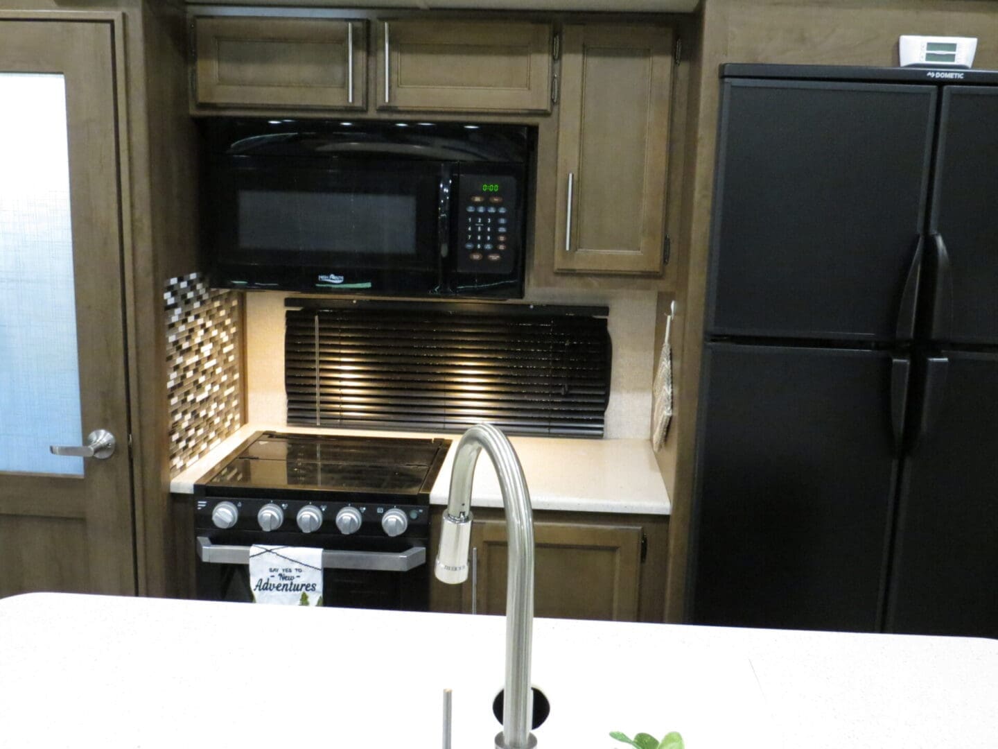 A modern kitchen with dark wood cabinets, stainless steel refrigerator, microwave, and a sink with a high faucet, viewed over a countertop.