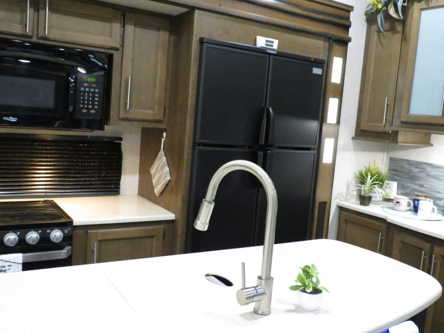 A modern kitchen with dark wood cabinets, a black refrigerator, and stainless steel appliances, including a prominent faucet and oven.