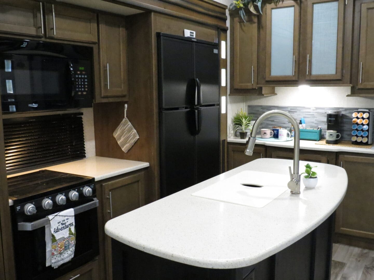 Modern kitchen interior with dark wood cabinets, stainless steel appliances, and an island with a white countertop.