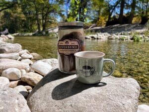 A Jar of ground coffee from Riverbend Roasted coffee along with a Frio River coffee mug on rocks in the Frio River.